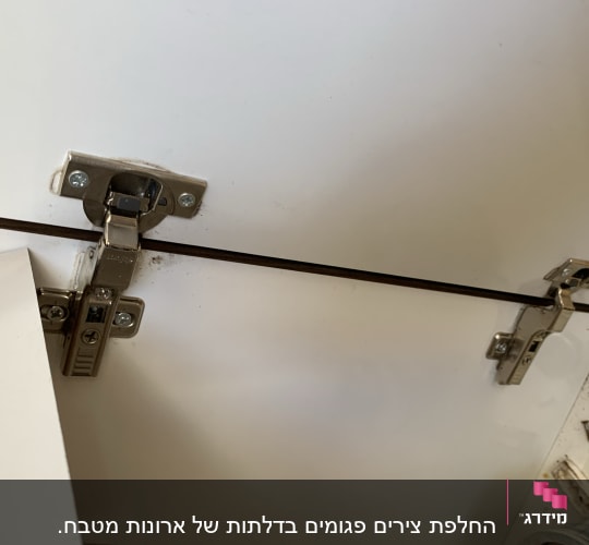 צירי מתכת מותקנים על דלת ארון מטבח לבנה